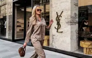 Blonde woman wears OLA VOGA satén komplet, shirt and pants, walking past YSL boutique storefront.